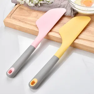 Large silicone baking spatulas in pink and yellow on a wooden cutting board