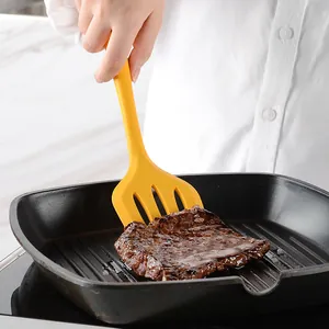 Espátula ranurada de silicona amarilla de calidad volteando un filete en sartén grill