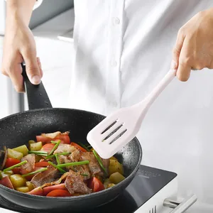 Ergonomic light pink silicone slotted turner kitchen spatula being used for stir-frying food in pan