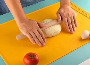 Detailansicht von Händen, die Teig auf einer gelben Silikon-Backmatte ausrollen.