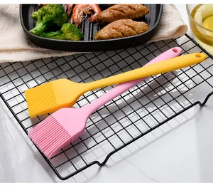 Two colorful silicone basting brushes on a black rack with grilled food in background.