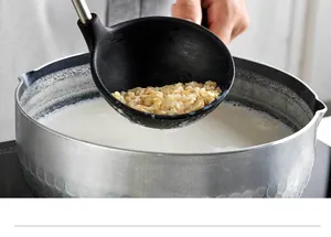Gros plan d'une louche en silicone noire puisant du porridge d'avoine dans un pot argenté martelé