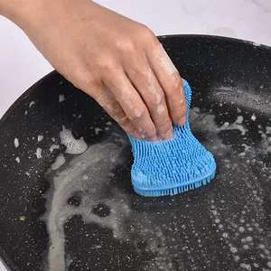 Flexible blue soap-shaped silicone dishwashing brush cleaning a black pan with foam