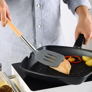Heat-resistant silicone spatula with wooden handle flipping chicken in a square grill pan