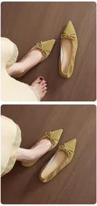 Close-up of mustard yellow suede pointed-toe ballet flats with bow detail on wood floor