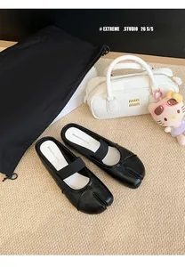 Black leather split-toe Tabi mules with elastic strap, shown with lifestyle accessories