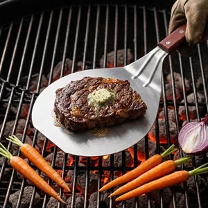 Professional large stainless steel BBQ spatula with wooden handle holding a grilled steak
