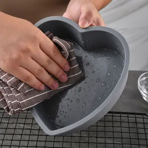 Large heart-shaped grey silicone cake mold for baking being cleaned with a brown cloth
