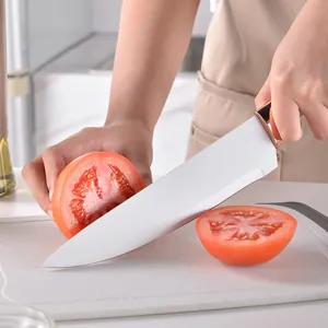 Chef knife with white blade and gold bolster slicing fresh tomato on cutting board