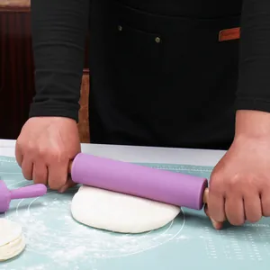 Purple silicone rolling pin with wooden handles rolling dough on a blue mat