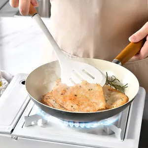 White silicone slotted turner with wooden handle used for frying meat in a pan