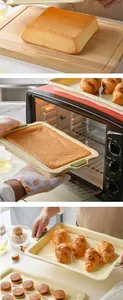 Detail view of cream silicone baking pans with green handles used in a kitchen oven.