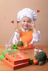 Asiatischer kleiner Koch posiert mit Karotten-Silikon-Baby-Geschirr-Set für Kleinkinder