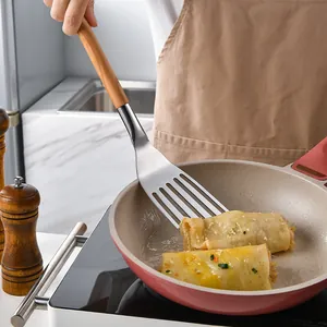 Espátula para pescado de acero inoxidable con mango de madera volteando comida en sartén