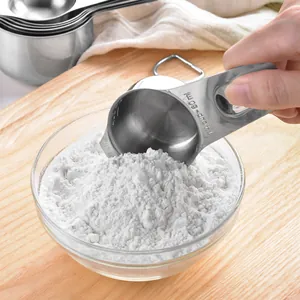 Professional stainless steel measuring cup set for baking, shown scooping flour in a kitchen