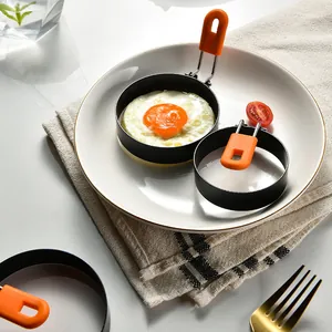 Non-stick round egg frying ring with orange silicone handle on a breakfast plate