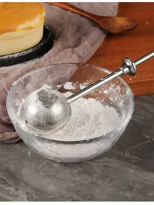 Detailed close-up of stainless steel retractable duster in bowl with powdered sugar