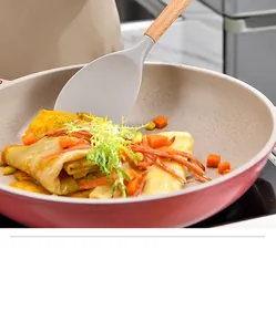 Detailed close-up of a silicone spatula with wooden handle in a non-stick frying pan