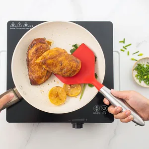 Wide red silicone spatula with stainless steel handle used for flipping chicken in pan