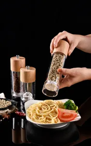 Hand using manual oak pepper grinder over a plate of delicious pasta with herbs.