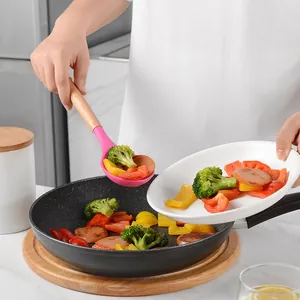 Roze siliconen kooklepel met houten handvat die verse groenten uit een pan schept