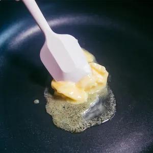 Espátula de silicona revolviendo mantequilla derretida en una sartén antiadherente