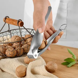 Stainless steel nutcracker tool being used to crack walnuts on a wooden board.
