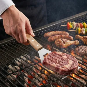 Espátula de barbacoa de acero inoxidable con mango de madera volteando un filete en parrilla