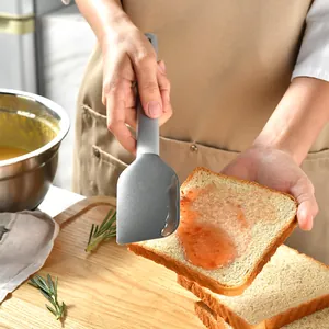 Gray silicone spatula spreading strawberry jam on a slice of toasted bread