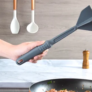 Schiacciacarne manuale grigio per carne macinata tenuto sopra una padella in cucina