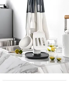 Set di 13 utensili da cucina in silicone bianco appesi a un supporto rotante moderno.