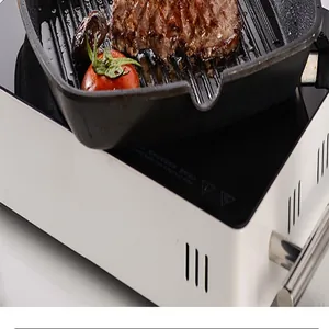 Close-up of a square grill pan with steak and tomato cooking on a white induction stove