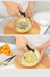 Manual stainless steel potato masher mashing potatoes in a clear bowl on a wooden board