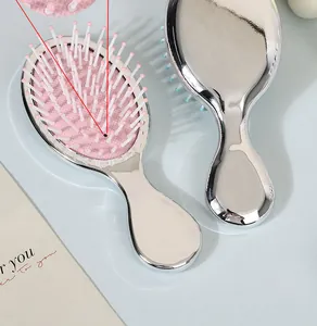 Detailed view of a mini silver metallic air cushion hairbrush with pink massage bristles