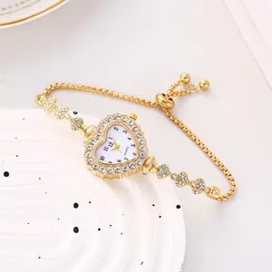 Dettaglio di un orologio a cuore dorato con strass e cinturino a scorrimento regolabile.