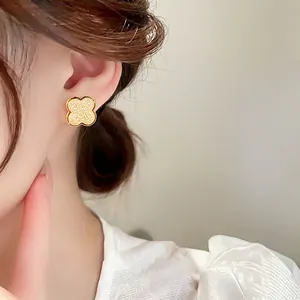 Close-up of gold frosted four-leaf clover stud earring worn by a model.