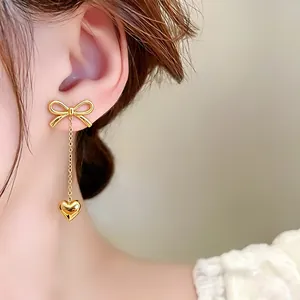 Close-up of elegant gold bow earrings with delicate heart tassels worn by a model.