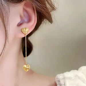 Elegant gold-tone heart drop earrings featuring radiant texture on model's ear