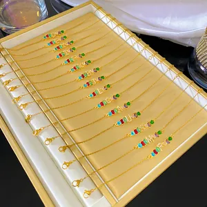 Primer plano de elegantes pulseras de iniciales con piedras de arcoíris y 26 letras doradas.