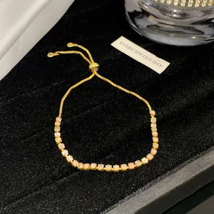 Nahaufnahme eines vergoldeten Armbands mit zarten rosa und weißen Zirkonsteinen.