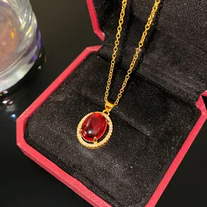 Gros plan d'un collier en or avec pierre rouge et halo de zircons dans un écrin rouge.