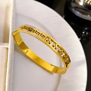 Close-up of gold titanium steel bangle with hollow Greek key and four-leaf clover motifs.