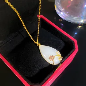 Close-up view of a teardrop faux jade necklace with gold floral design in box