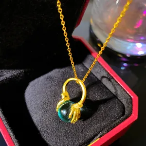 Close-up of unique golden hands holding a green orb pendant necklace in a red gift box