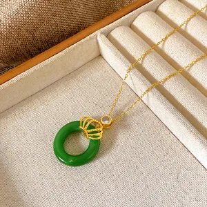 Close-up detail of golden titanium steel necklace with crown charm and green round pendant