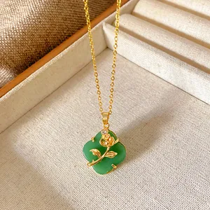 Detail shot of a green clover pendant necklace with a gold rose motif in a jewelry tray