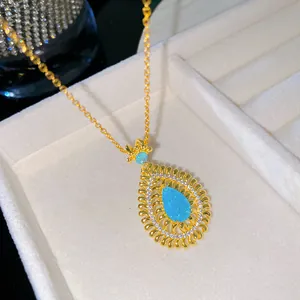 Macro view of a gold teardrop pendant necklace featuring a vivid blue turquoise stone