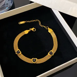 Detailed view of gold titanium steel mesh bracelet with black heart charms in a box.