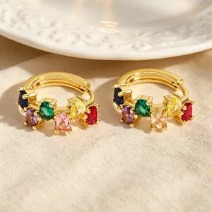 Close-up of gold-plated huggie earrings with colorful oval-shaped zircons.