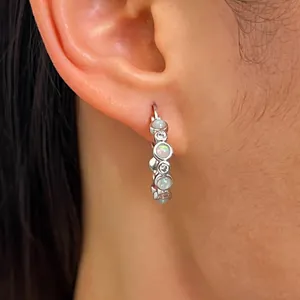 Close-up of silver hoop earrings featuring iridescent opal stones and sparkling cubic zirconia.